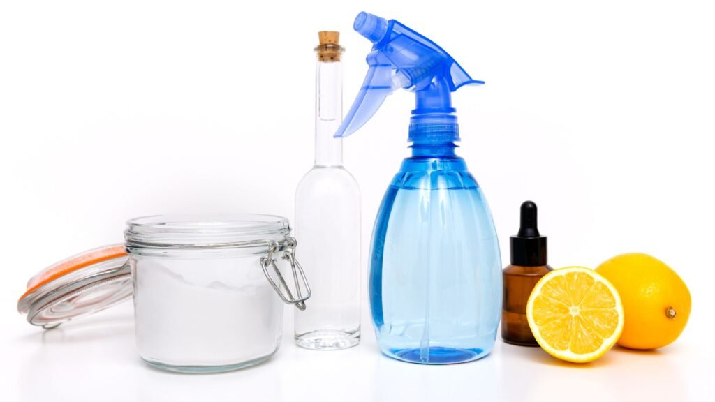 Ingredientes de misturinha caseira perigosas: bicarbonato, vinagre, limão, borrifador azul e frasco de essência sobre fundo branco.