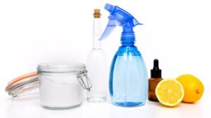 Ingredientes de misturinha caseira perigosas: bicarbonato, vinagre, limão, borrifador azul e frasco de essência sobre fundo branco.
